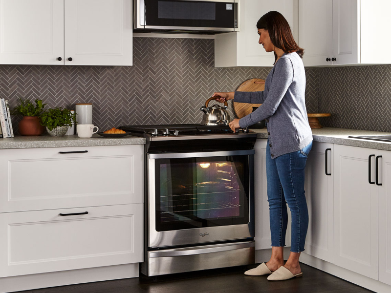 A woman standing next to a Whirlpool® oven in a modern kitchen. A woman standing next to a Whirlpool® oven in a modern kitchen.