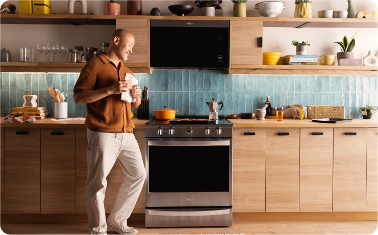 A person walking through a modern kitchen with light wood cabinets and Whirlpool brand appliances