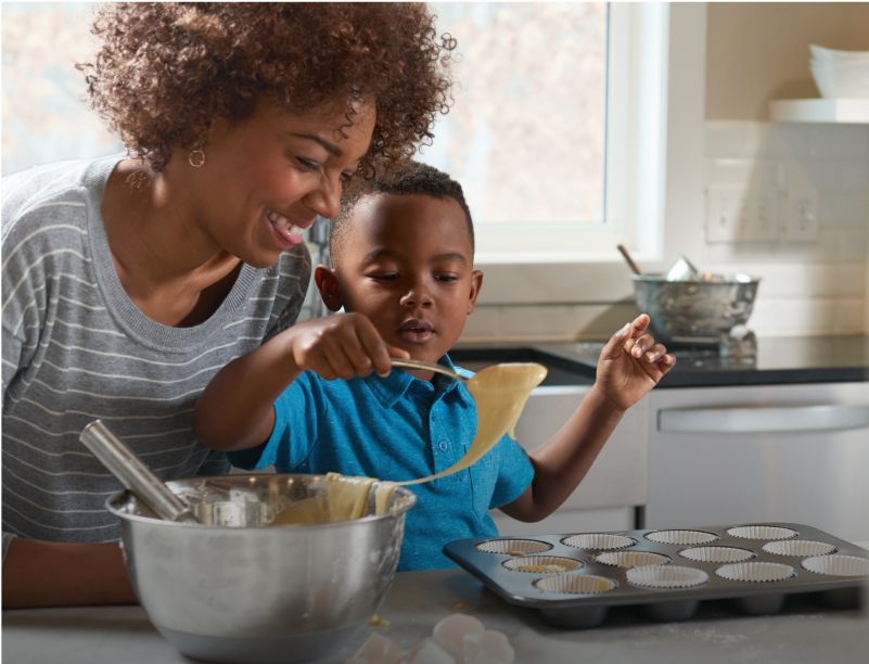 An adult and a child fill a cupcake tin with batter
