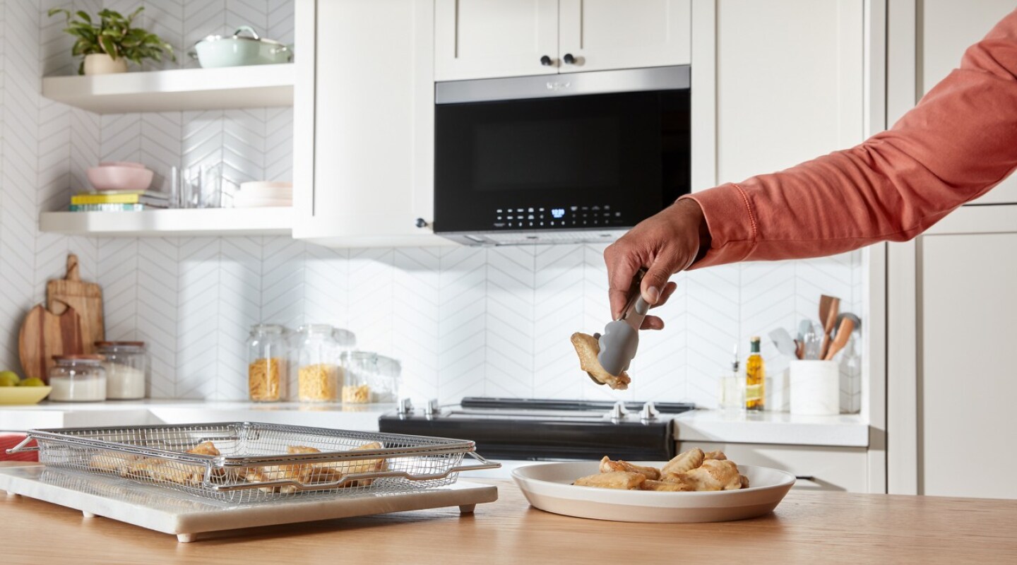 A person using tongs to place chicken wings in an air fry basket
