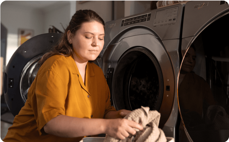 A person in a yellow blouse loading a dark gray washing machine at home