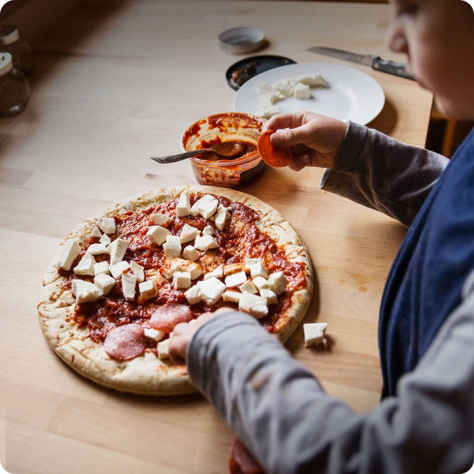 A child topping a pizza with cheese and pepperoni