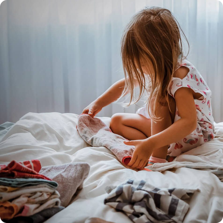 A child sitting on a bed while folding small towels