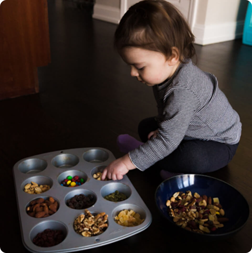 A toddler sorting trail mix in a muffin tin