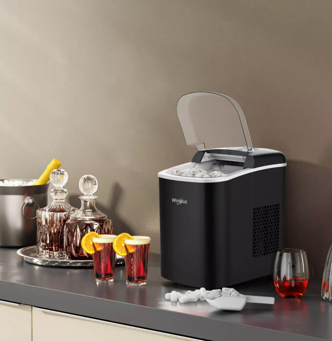 A Whirlpool® Ice Maker sitting on a counter with cold beverages placed next to it. A Whirlpool® Ice Maker sitting on a counter with cold beverages placed next to it.