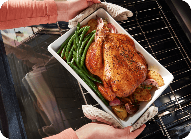Person pulling a roasted chicken and vegetables out of a Whirlpool® Range
