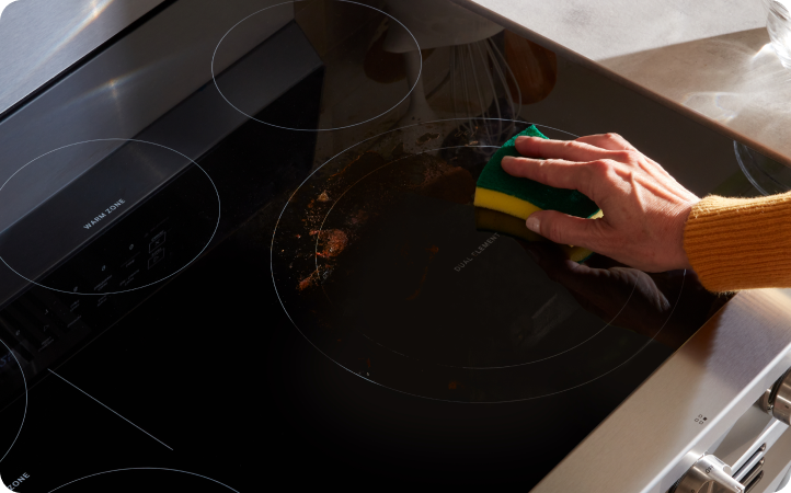 Someone scrubs the cooktop of a Whirlpool Oven with a sponge