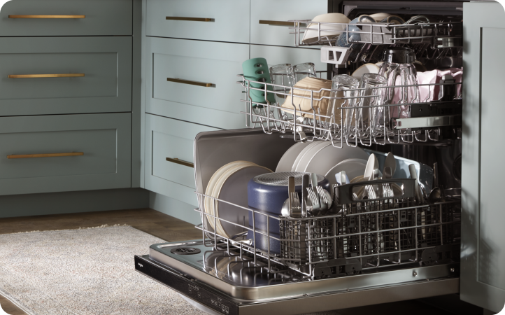 In a kitchen with grey cabinets is a dishwasher. It's opened and the racks are pulled out. Each rack is full of items like dishes, bowls, cups and more