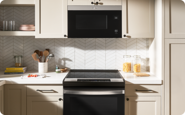 A kitchen with a Whirlpool Range and over-the-range microwave. On the counters are a full utensil holder, containers of pasta, cookbooks and other various items
