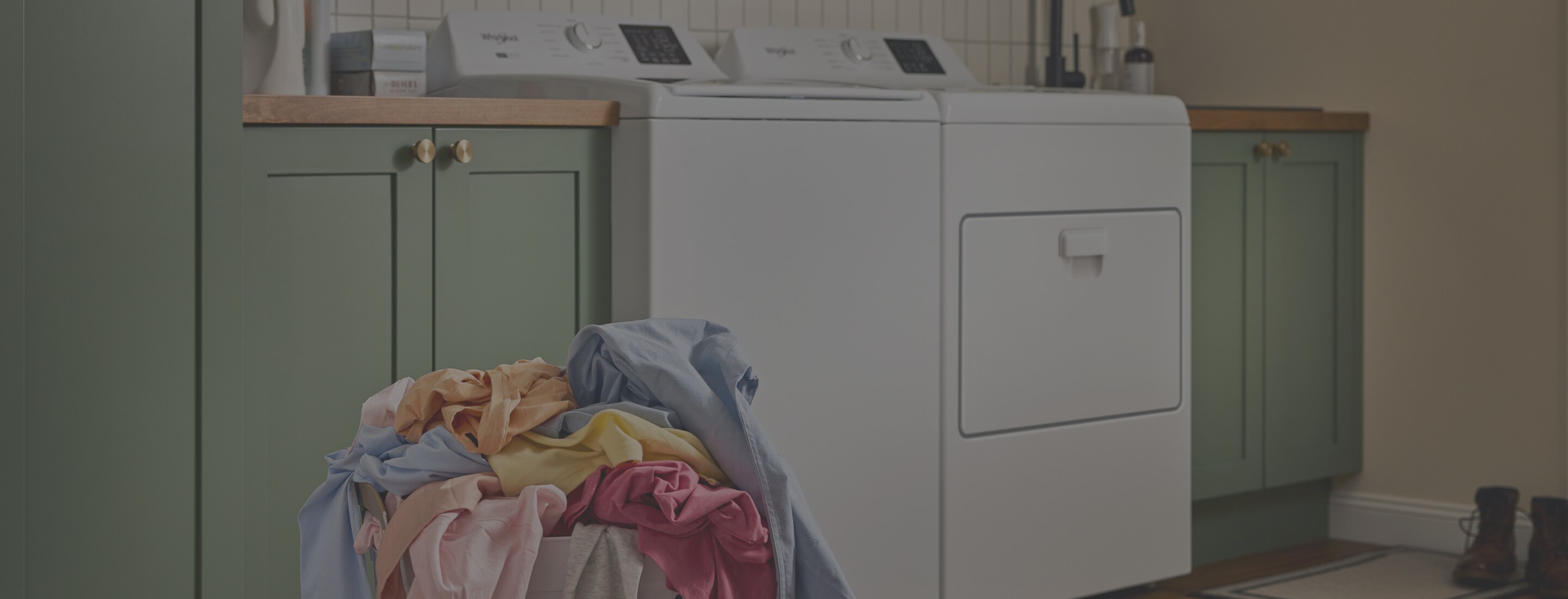 A person loads laundry in a Whirlpool® Top Load Washer and Dryer set