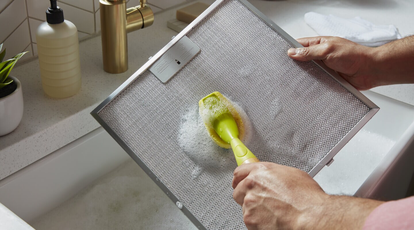 Person scrubbing a filter from a range hood Person scrubbing a filter from a range hood