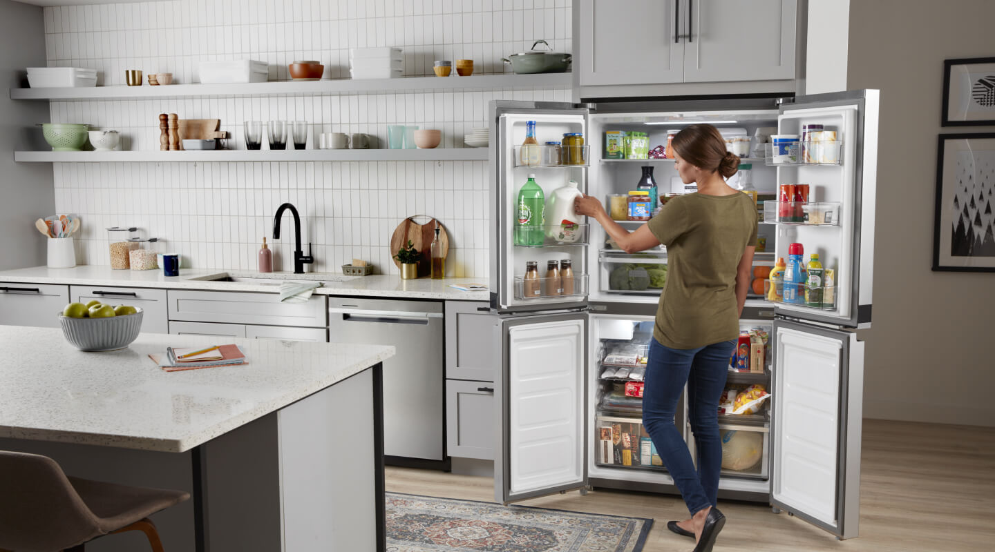 Person standing in front of an open fridge, removing items Person standing in front of an open fridge, removing items