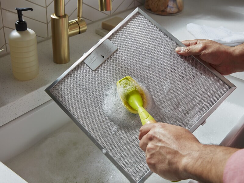 Person scrubbing a filter from a range hood
