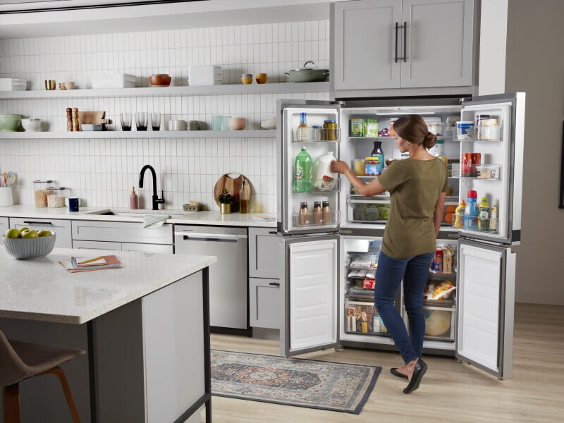 Person standing in front of an open fridge, removing items Person standing in front of an open fridge, removing items