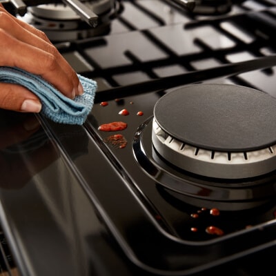 Person wiping up food splatter beneath grates on a gas stovetop