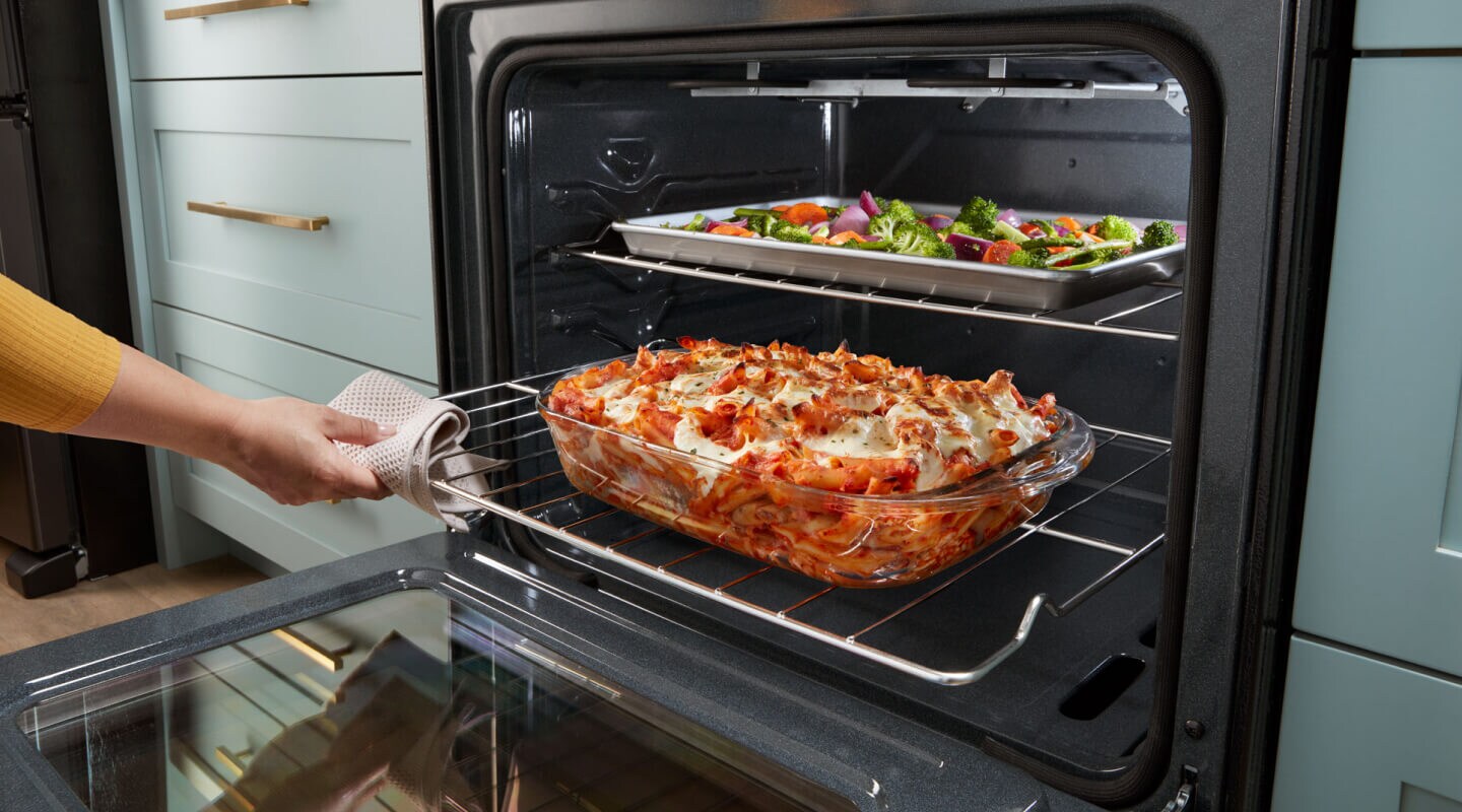 Person sliding out lower oven rack with lasagna on top Person sliding out lower oven rack with lasagna on top
