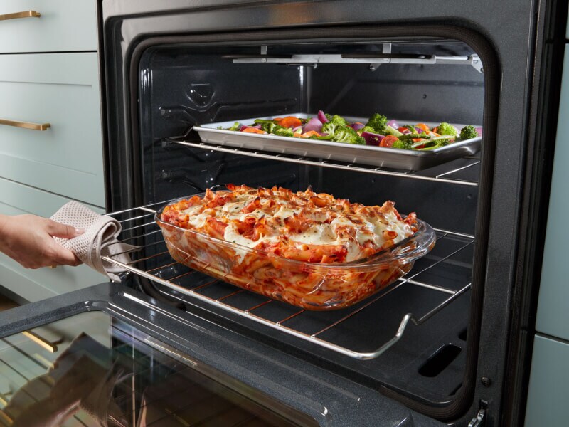 Person sliding out lower oven rack with lasagna on top Person sliding out lower oven rack with lasagna on top