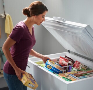 Woman placing food in white chest freezer baskets