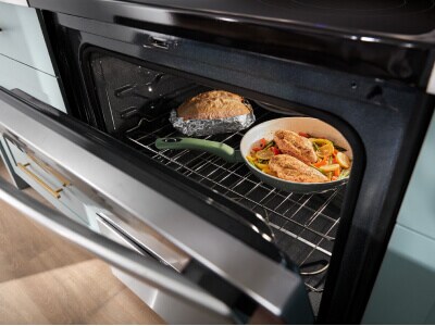 An oven door ajar exposing two dishes cooking inside