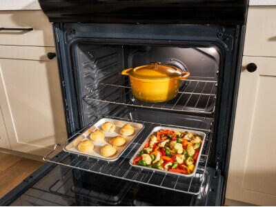 An open oven door exposing two pans with food in them and a closed Dutch oven
