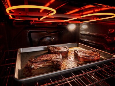 The inside of an oven with a pan of meat in it and the broiler coils lit up