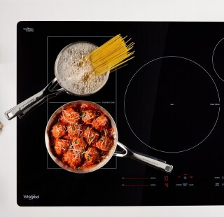 Pasta noodles boiling and meatballs simmering on a cooktop