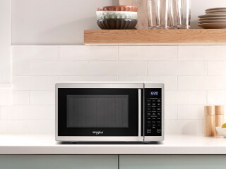 A countertop microwave underneath a brown shelf
