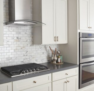 A cooktop and range hood surrounded by white cabinetry