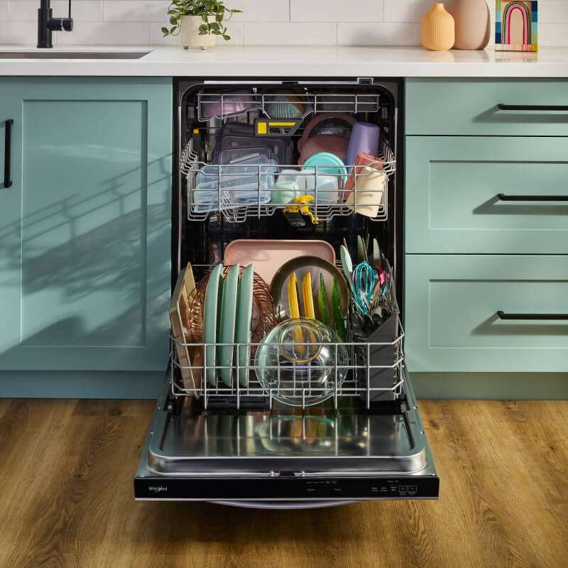 Open third rack dishwasher loaded with dishes between blue cabinets