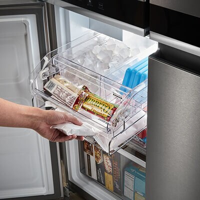 Person sliding ice drawer out of bottom-left 4-door compartment