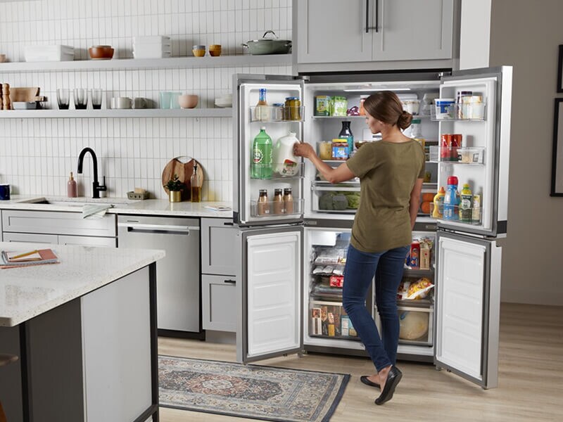 Person stocking the in-door shelving of an open Whirlpool® 4-Door Refrigerator Person stocking the in-door shelving of an open Whirlpool® 4-Door Refrigerator
