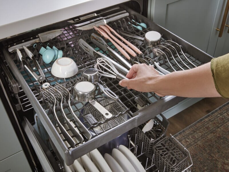 Person placing a whisk on a third-level dishwasher rack
