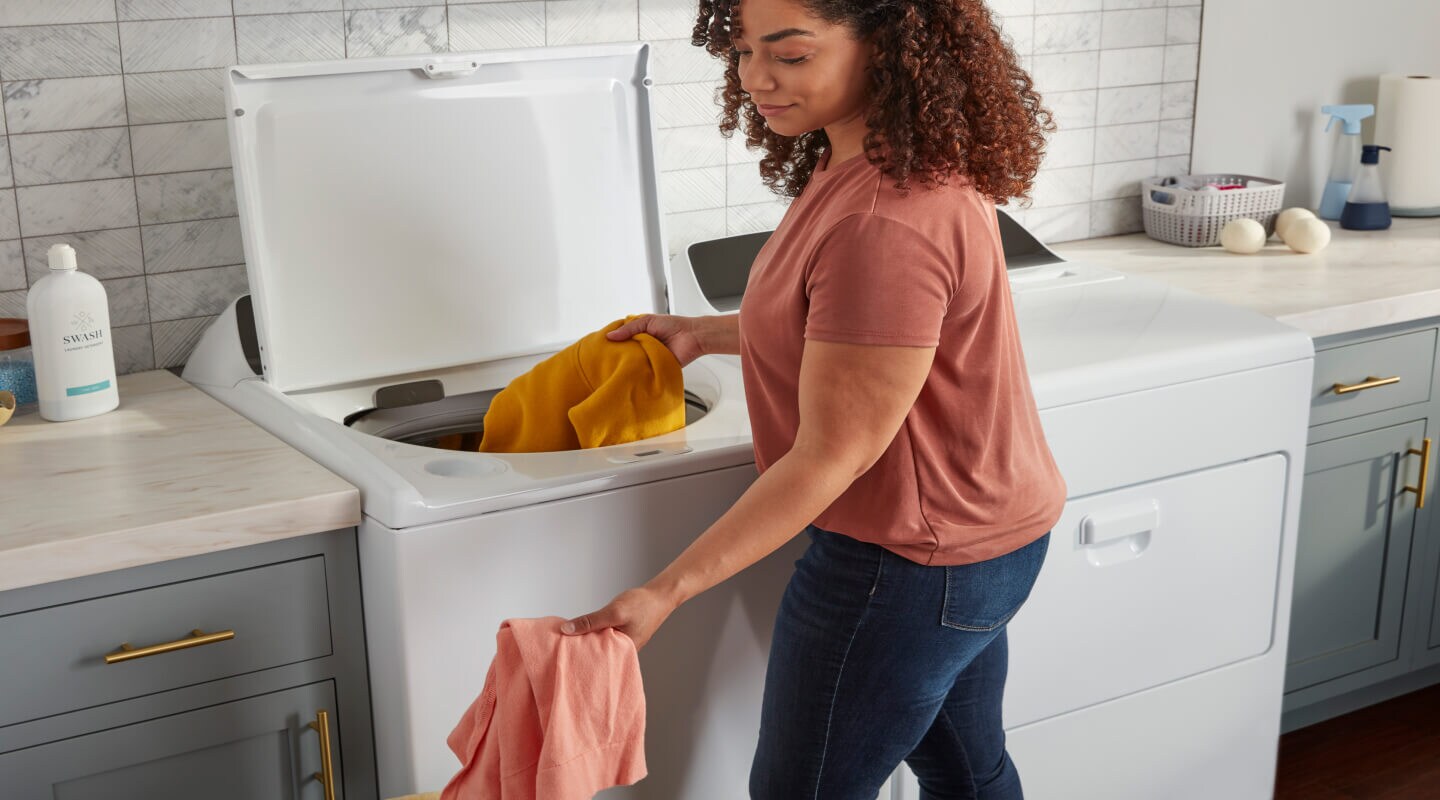 Person adding clothes to a white top load washer