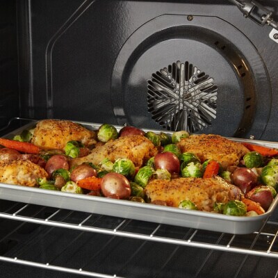 Chicken and vegetables on a baking sheet inside an oven