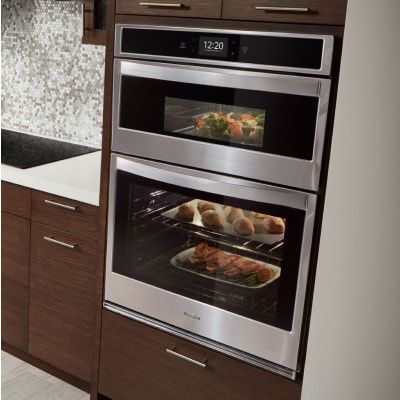 Whirlpool® stainless steel combination wall oven set into wood finished cabinets.
