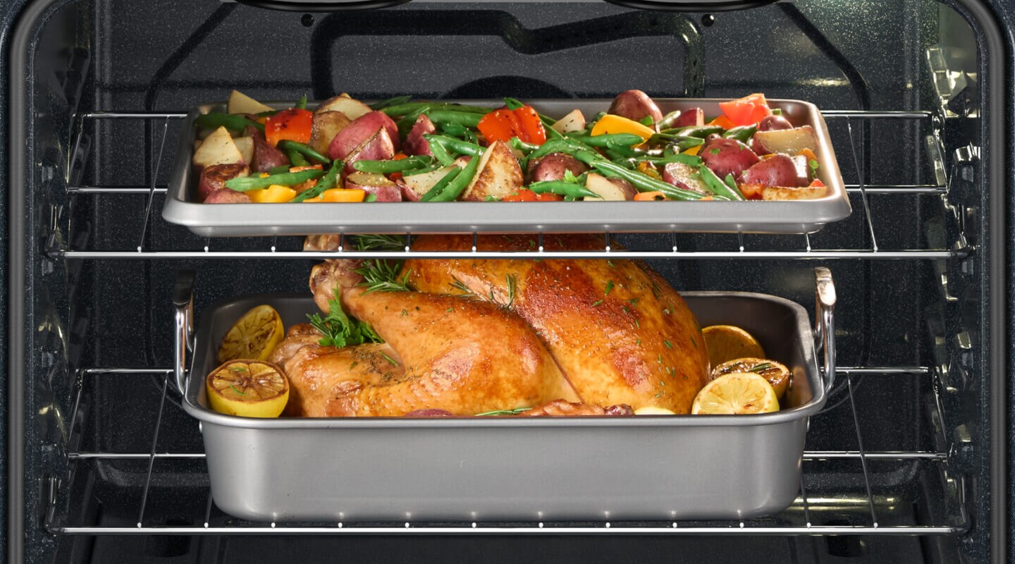A chicken and vegetables on different racks in an oven