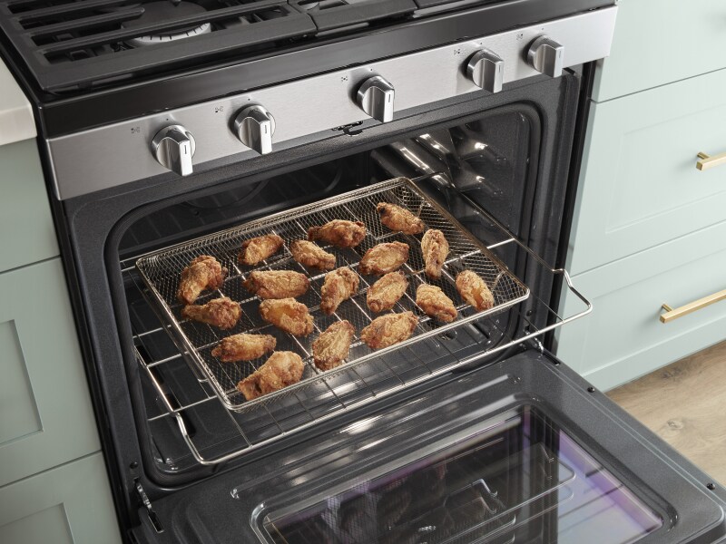 An open oven door with an air fryer basket containing chicken wings slid out. An open oven door with an air fryer basket containing chicken wings slid out.
