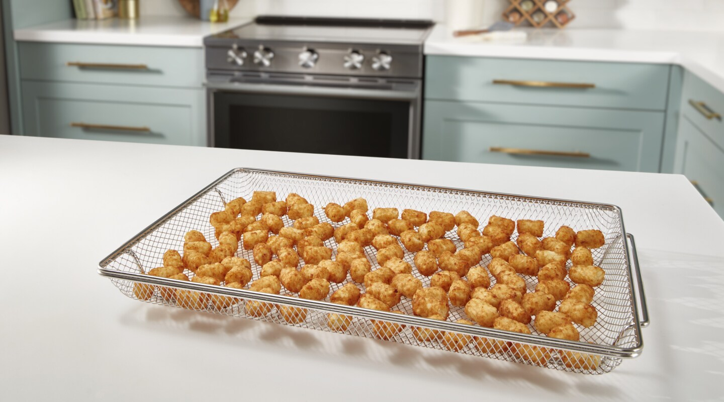 An air fry basket with tater tots sitting on a white countertop. An air fry basket with tater tots sitting on a white countertop.