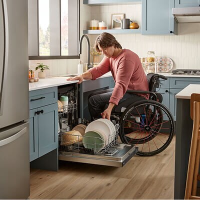 A person in a wheelchair unloading a Whirlpool® Dishwasher