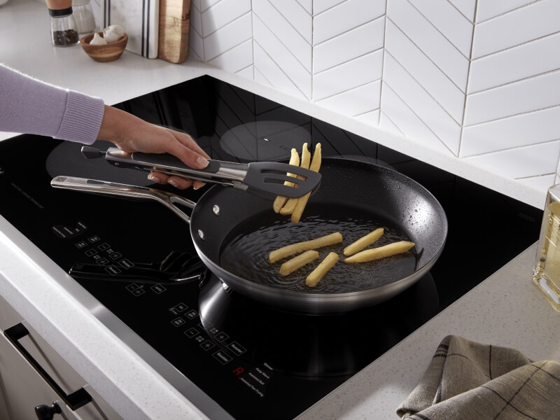 A person cooking French fries on an induction cooktop