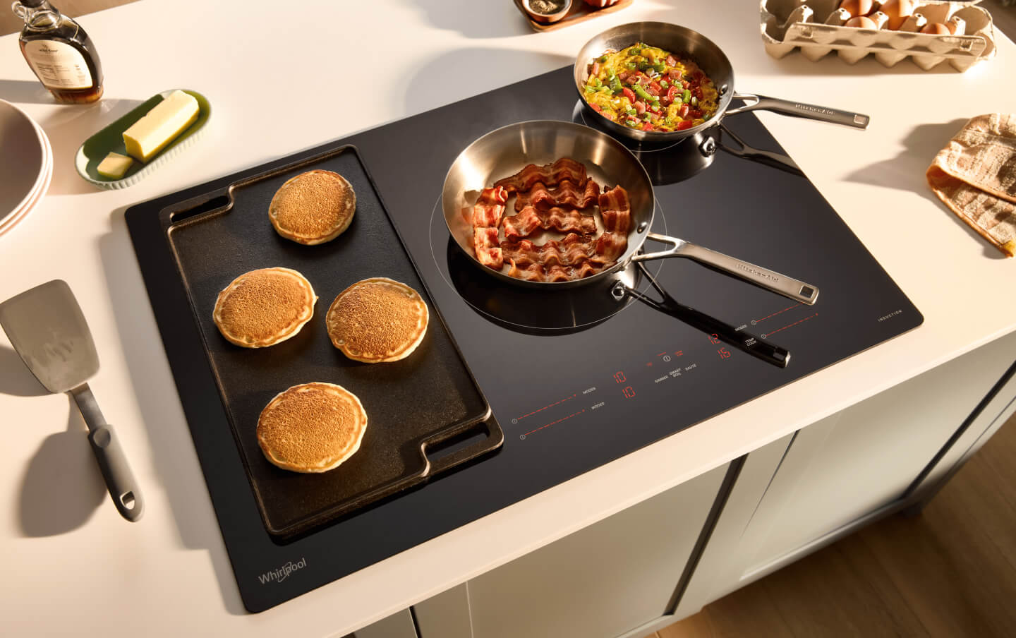 Breakfast food cooking in several pans on an induction cooktop