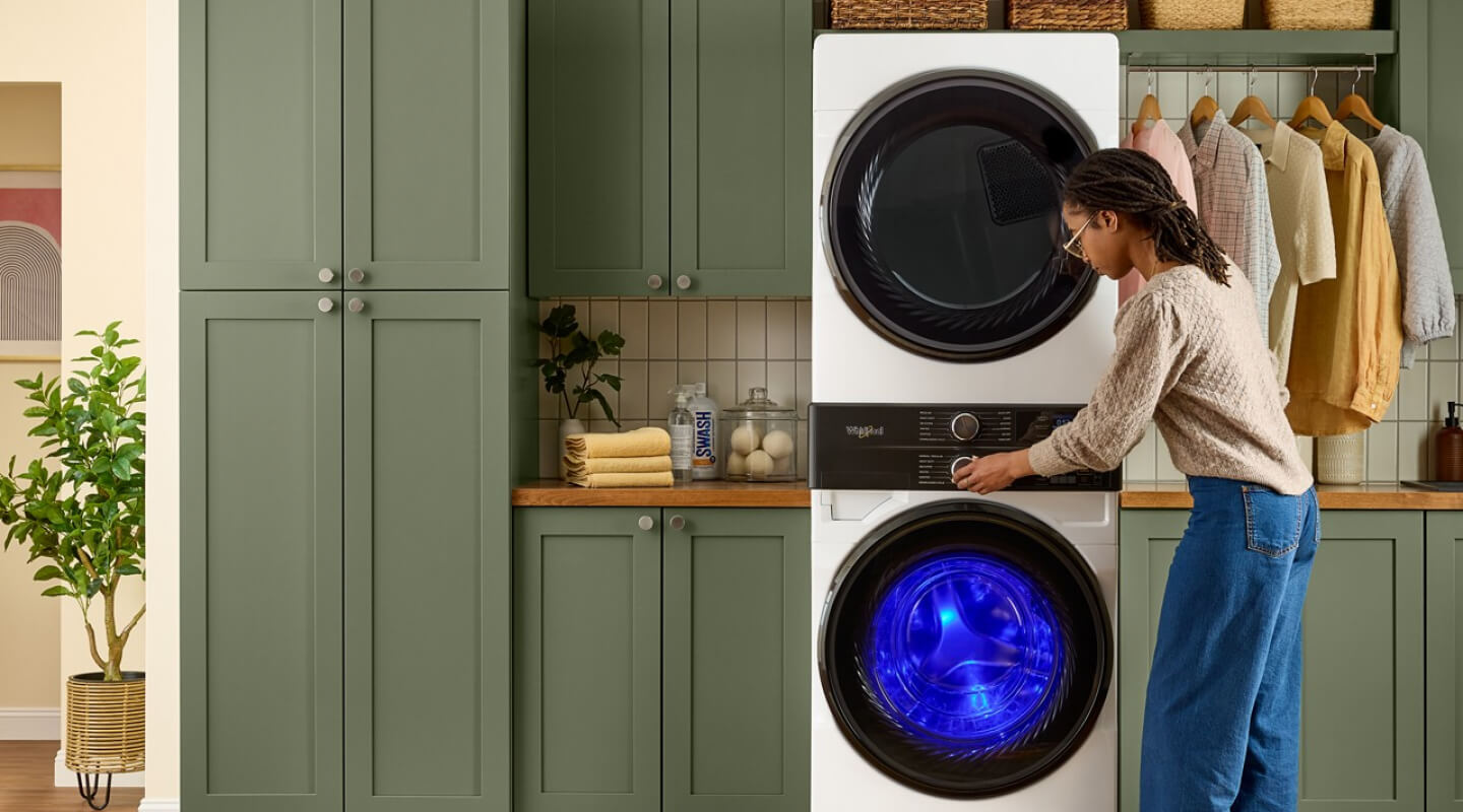 A woman adjusting the washer on her stacked unit in a home laundry area