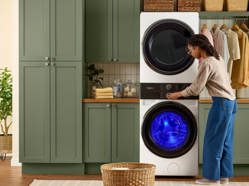 A woman adjusting the washer on her stacked unit in a home laundry area