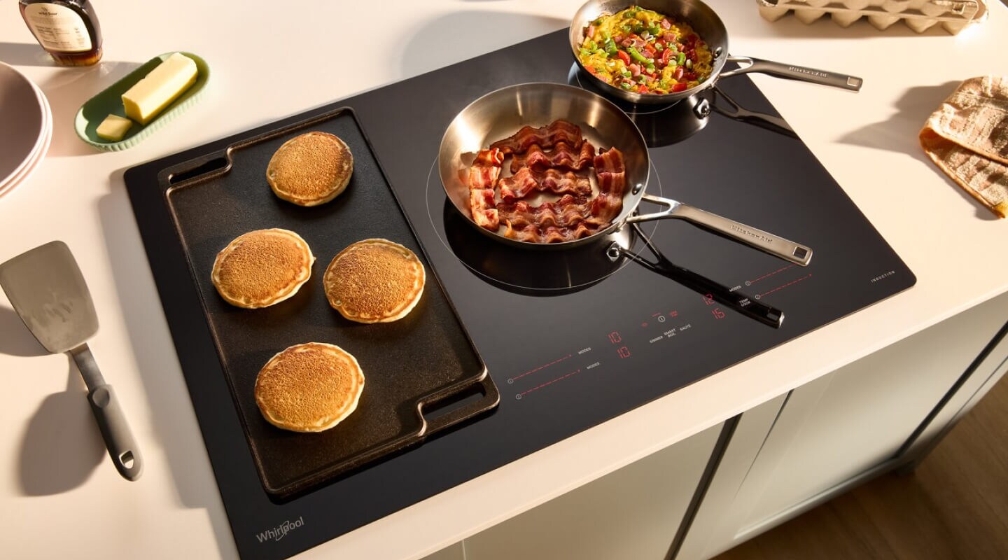 A smooth glass cooktop with pancakes and eggs cooking in pans