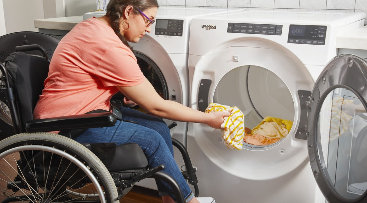 A person in a wheelchair putting clothes into a Whirlpool® Dryer A person in a wheelchair putting clothes into a Whirlpool® Dryer