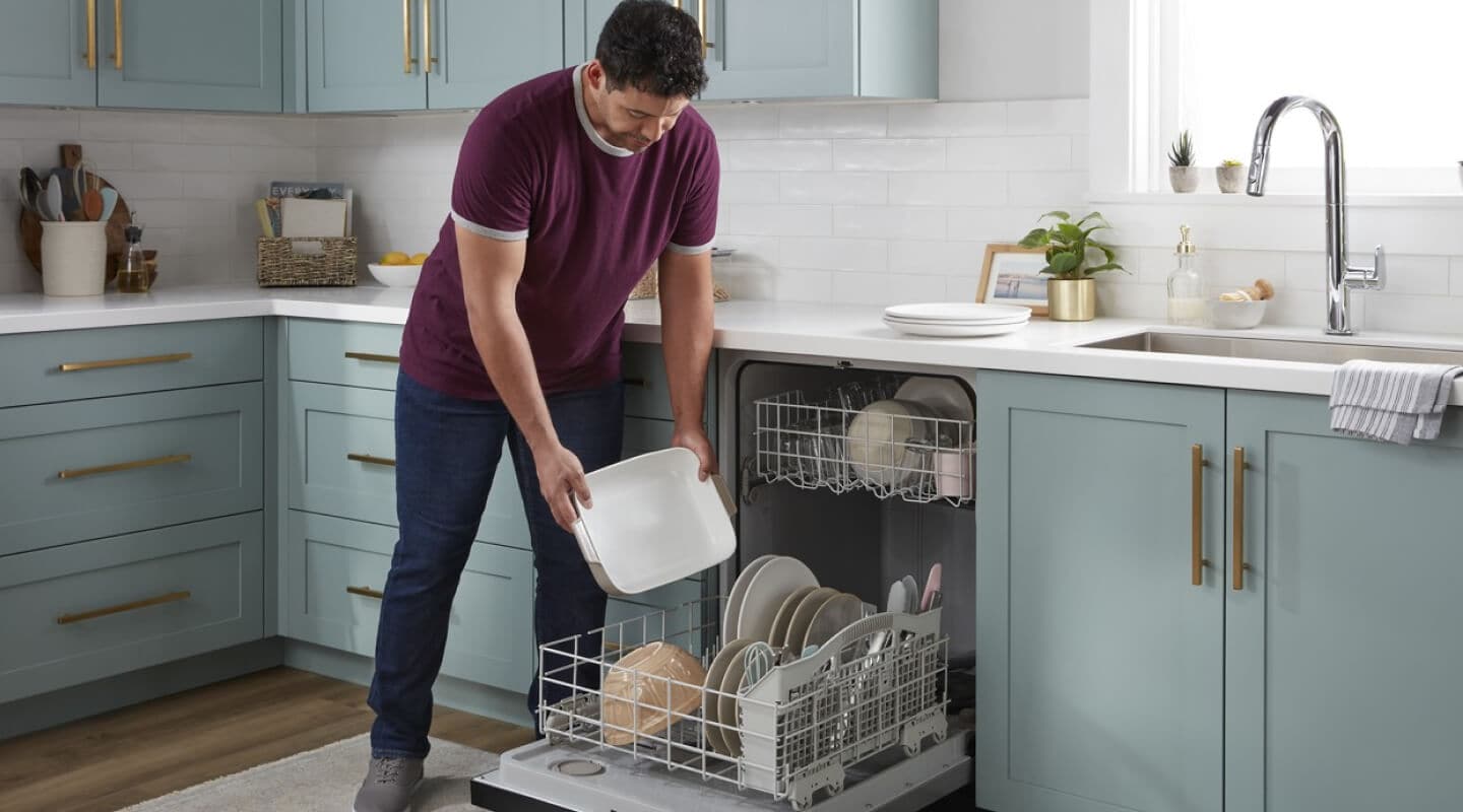 A person loading a Whirlpool® Dishwasher in a modern kitchen A person loading a Whirlpool® Dishwasher in a modern kitchen