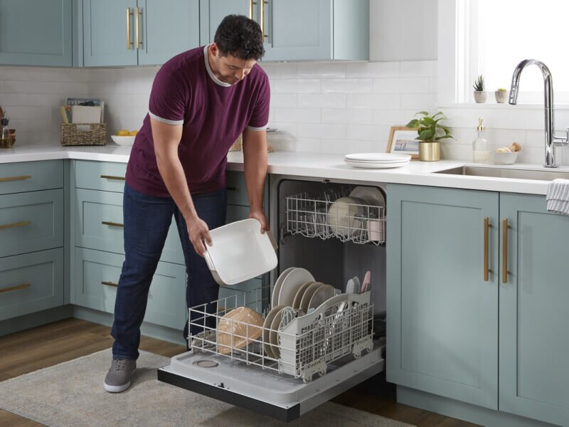 A person loading a Whirlpool® Dishwasher in a modern kitchen A person loading a Whirlpool® Dishwasher in a modern kitchen