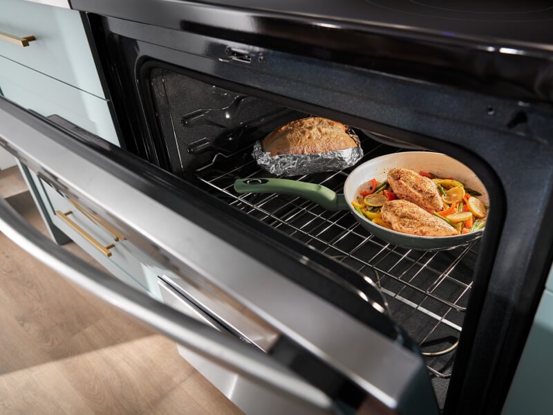 A chicken meal cooking in the oven with a loaf of bread