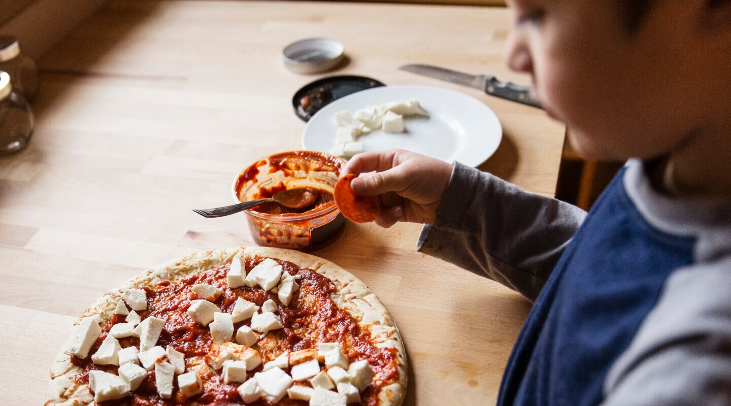 A kid placing toppings on a pizza A kid placing toppings on a pizza