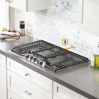 Gas cooktop set into gray countertop with measurements noted for distance between cooktop and wall